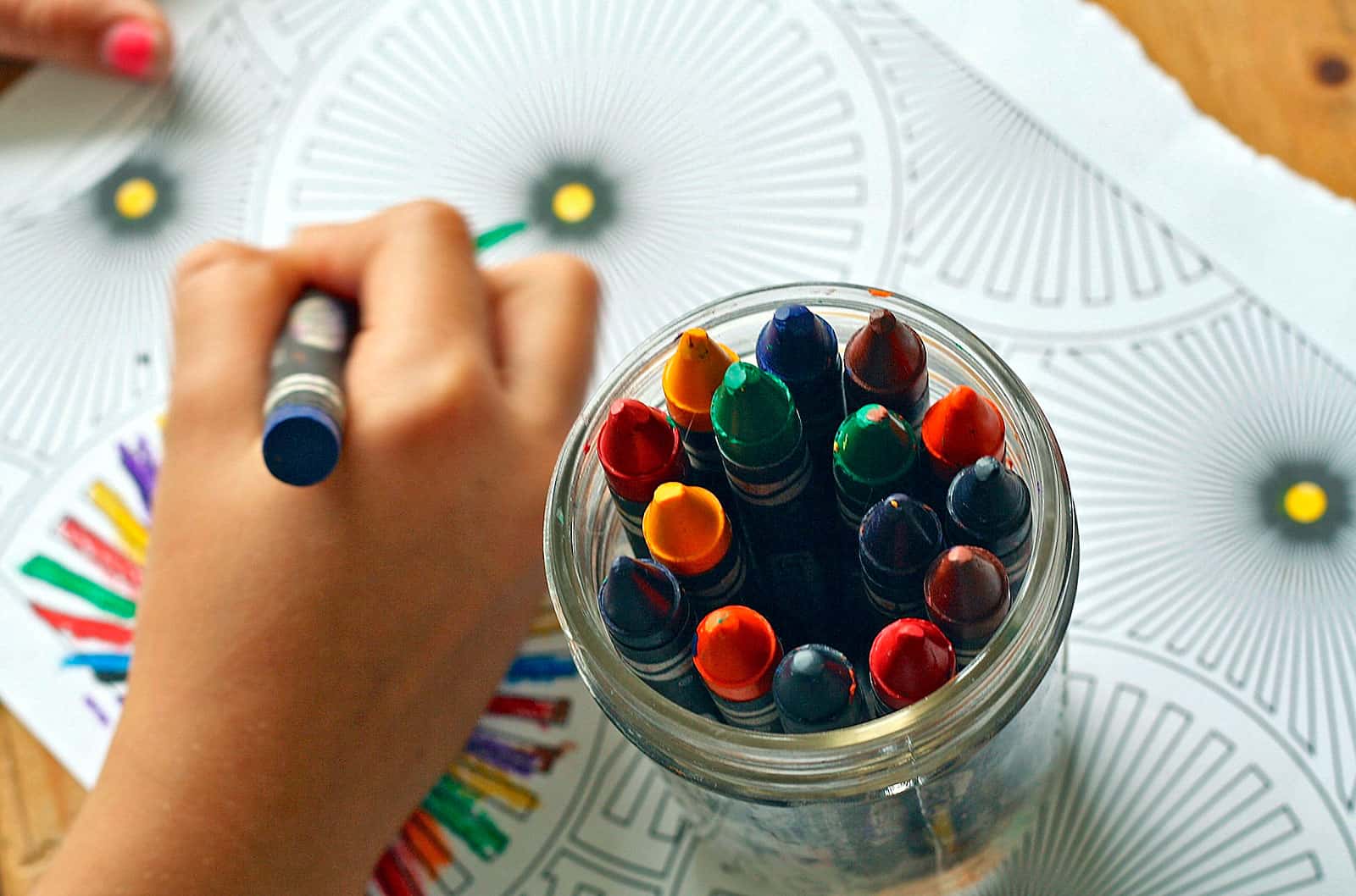 Copo com lápis de cor, sobre desenho com padrão simétrico para pintar na terapia de psicologia infantil.